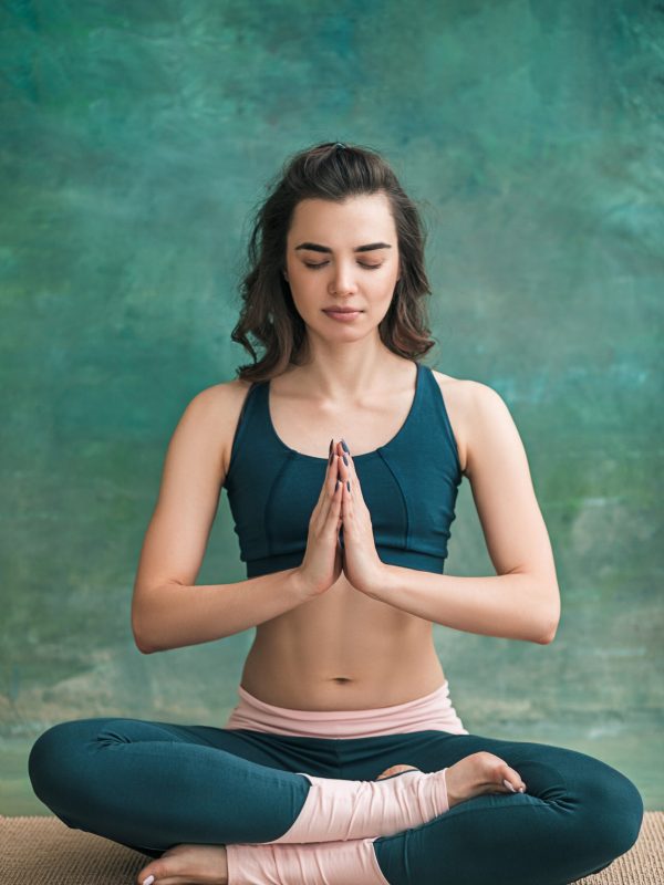 Studio shot of a young fit woman doing yoga exercises on green background